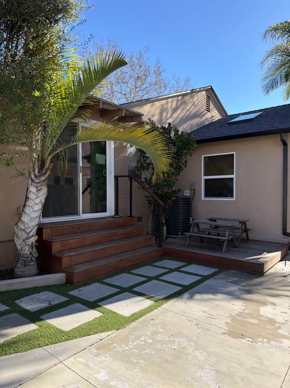 Back patio and deck entry with a paver path, picnic table, and palm trees