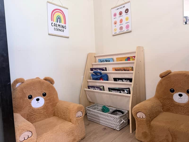 Calming corner with two plush bear chairs, a feelings chart, and a rack of picture books