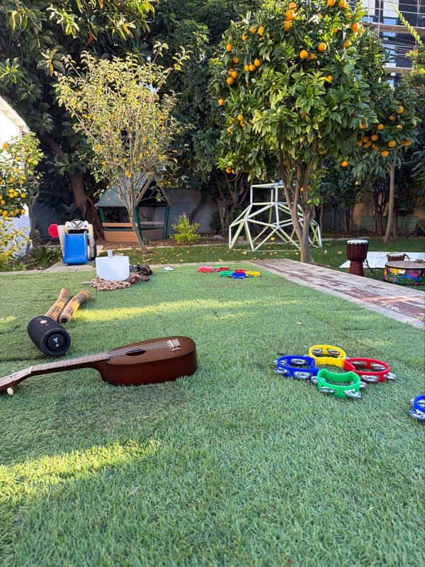 Music circle on the lawn with a small guitar, colorful tambourines, rhythm sticks, and a drum beneath an orange tree
