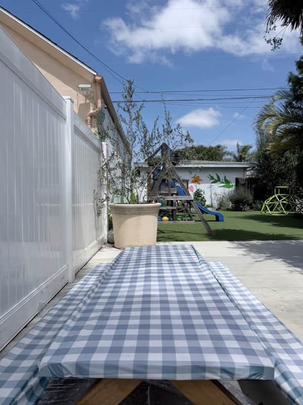 Gingham-covered picnic table on the patio, looking out at the lawn and play structure