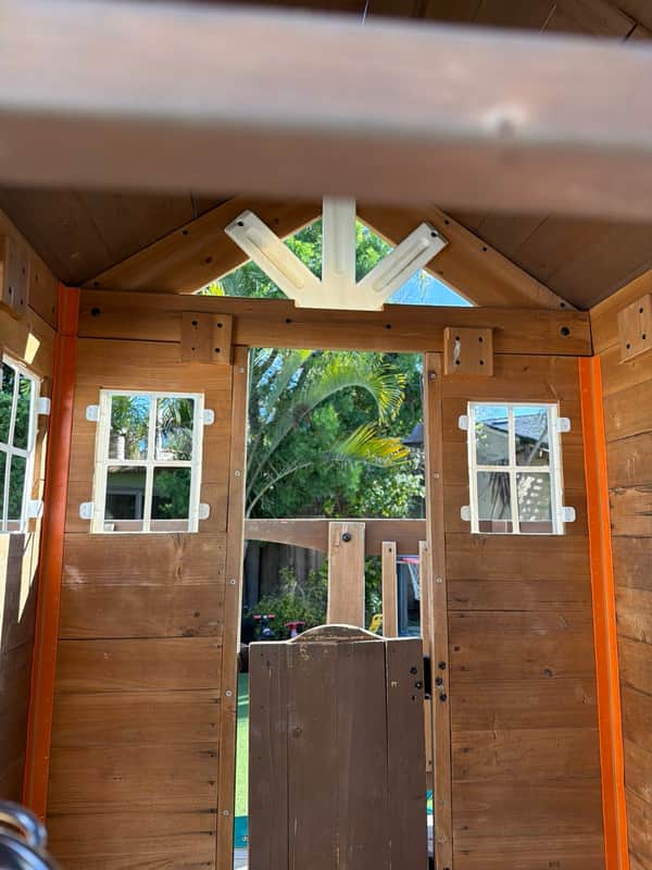 Inside the wooden playhouse, looking out paned windows to the palm-shaded yard