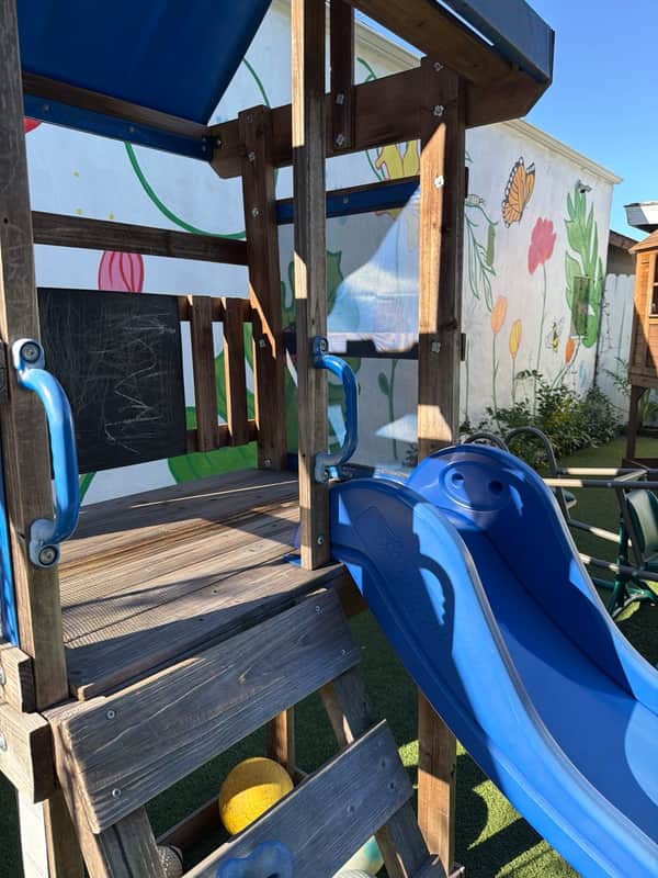 Play tower with a chalkboard panel and blue slide beside the flower mural